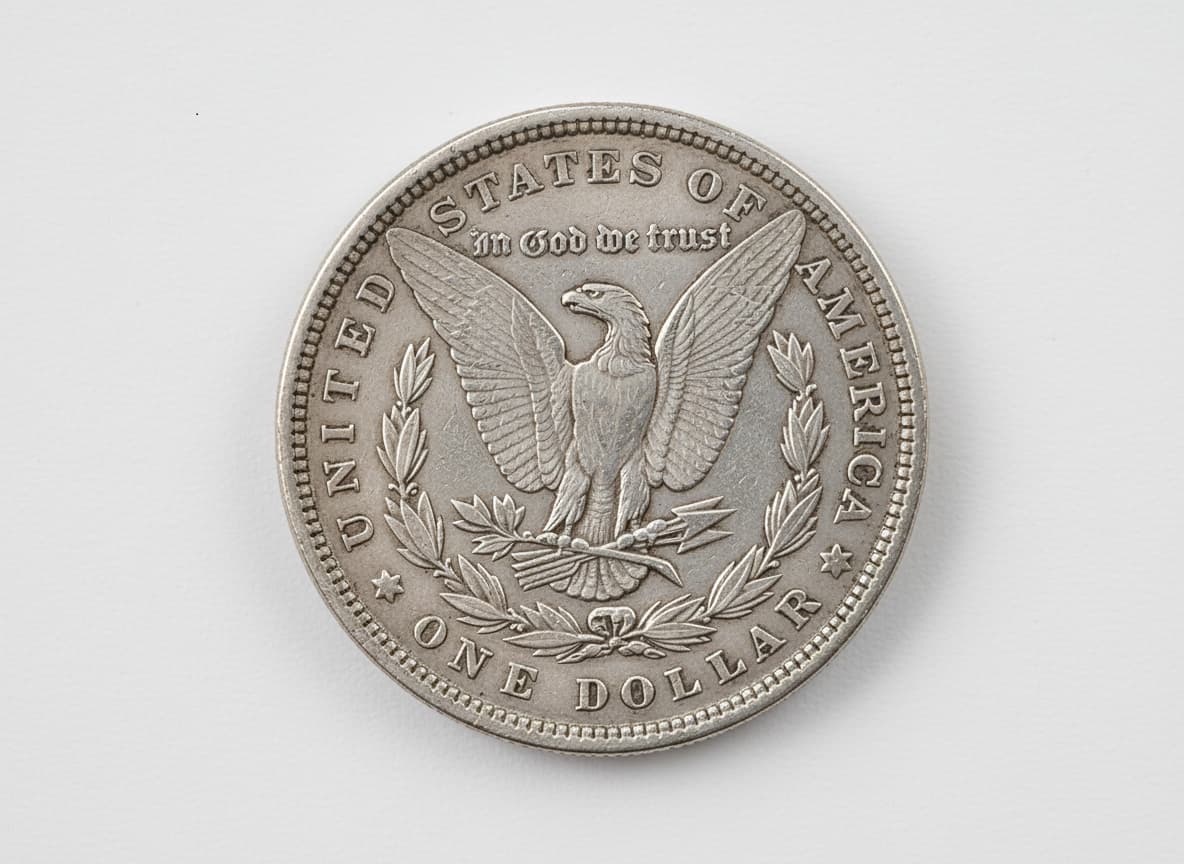 Reverse of a Morgan Silver Dollar coin laying flat on a white background