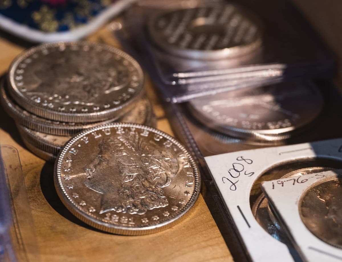 A collection of Morgan silver dollars and other silver coins in a wooden drawer