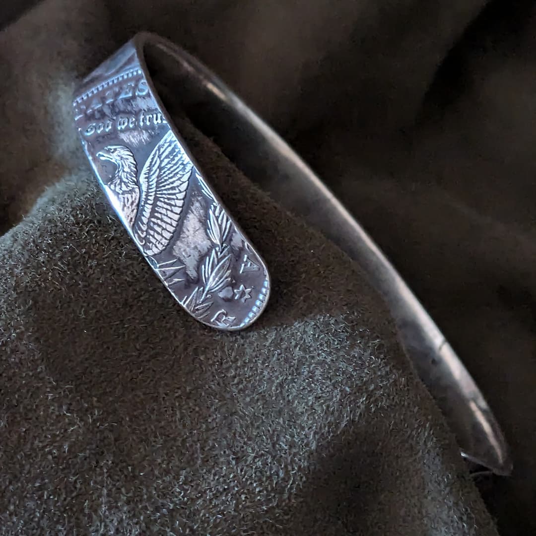 Silver bracelet with engraved design on a dark fabric background