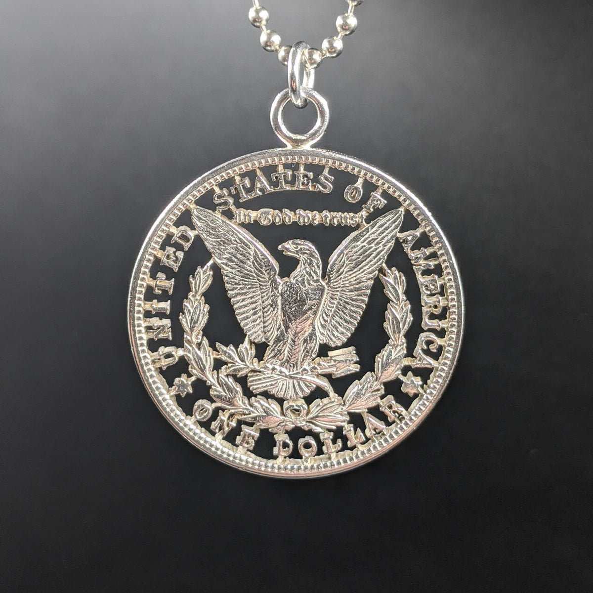 Morgan Silver Dollar coin with the background cut out with a jeweler's saw, hanging from a chain to form a pendant