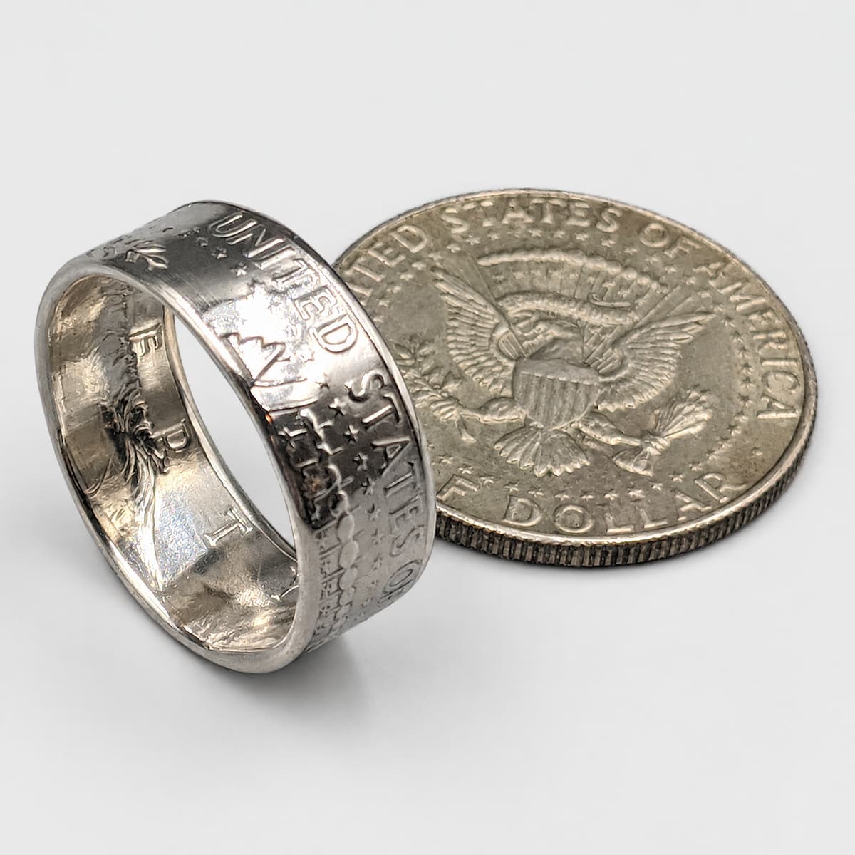 JFK Half Dollar Coin Ring from Silver State Foundry, with the coin in the background.