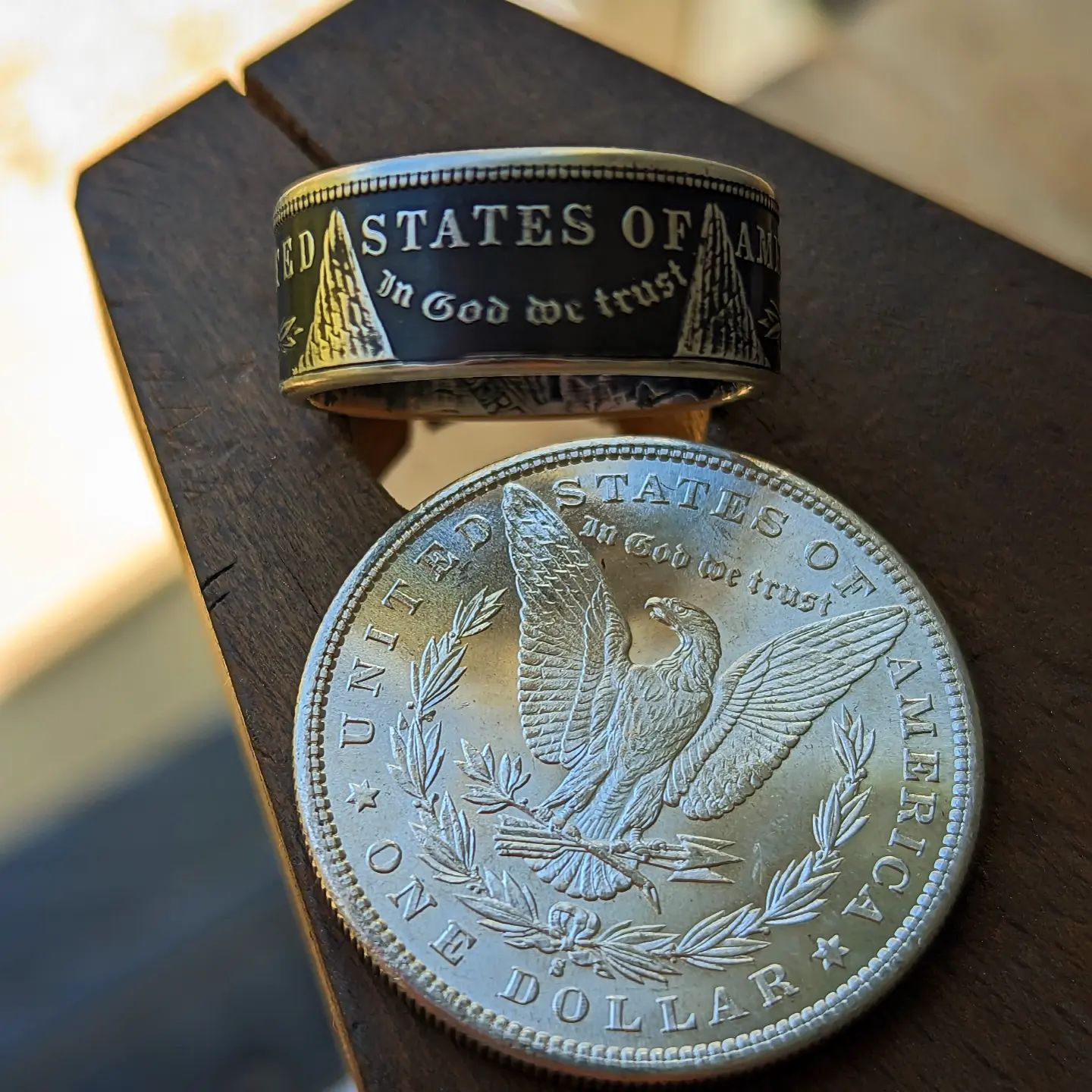 Morgan silver dollar coin ring with a patina finish and a silver dollar resting on a wooden bench pin