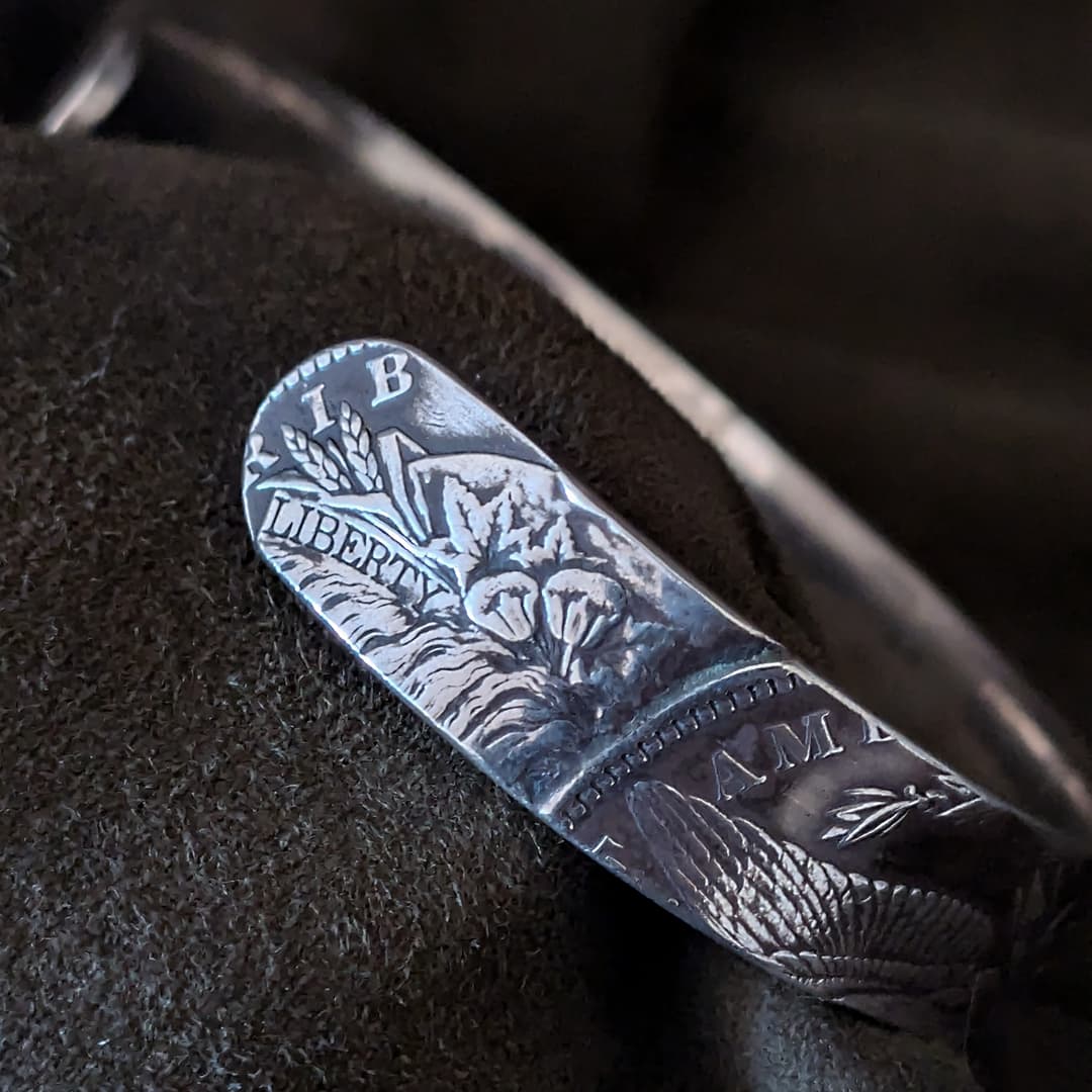 Close-up of a silver cuff with engraved design on a dark background