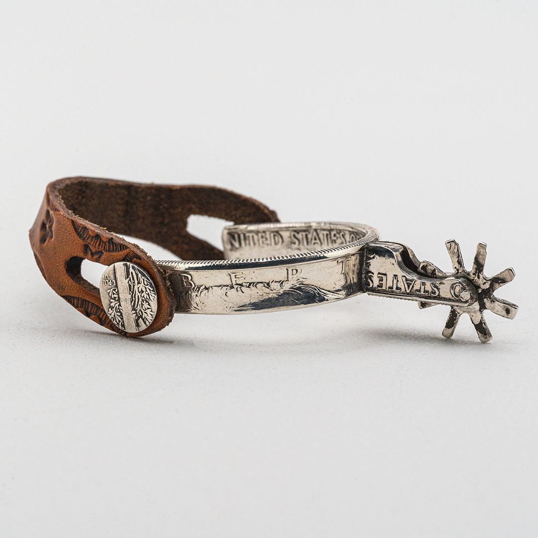 A tiny silver spur made from silver coins with hand tooled leather