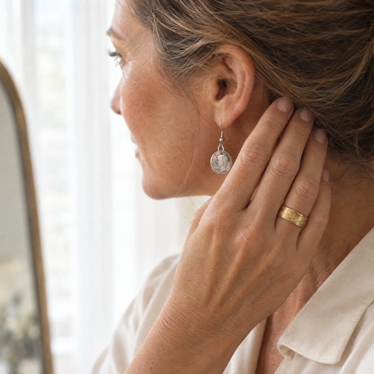 A woman wearing a gold coin ring on her hand and a mercury dime drop earing.