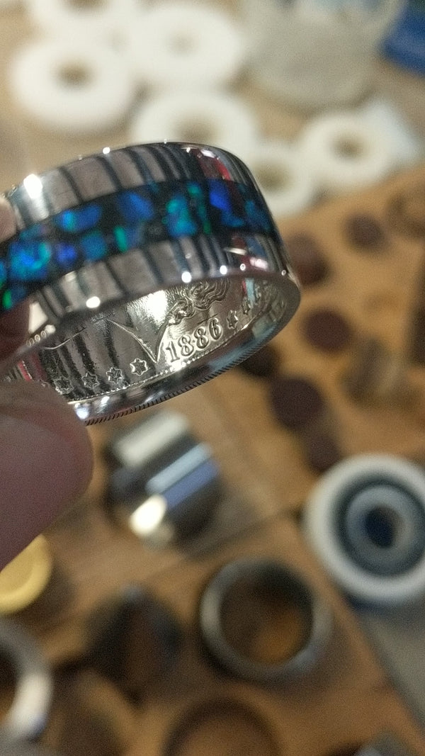 Video of a Morgan silver dollar coin ring with a blue and green opal inlay, slowly rotating to show how the opal catches and reflects the light.
