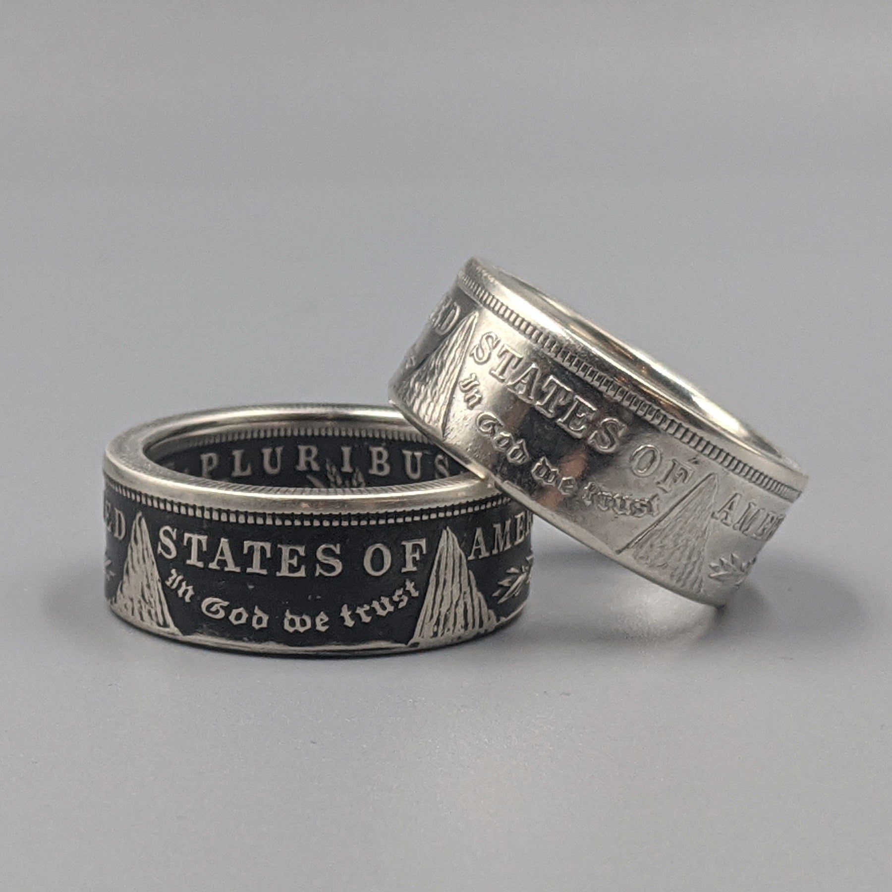 A pair of polished and patina-finished Morgan Silver Dollar coin rings on a white background.